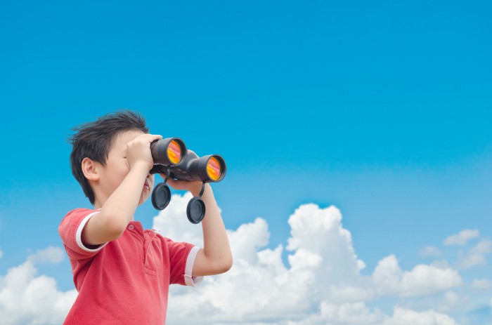 Boy looking through binoculars with the sky in the background